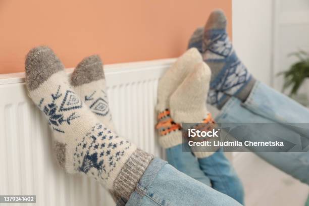 Family Warming Legs On Heating Radiator Near Color Wall Closeup Stock Photo - Download Image Now