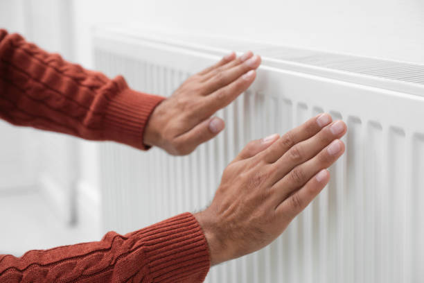 istock Man warming hands on heating radiator near white wall, closeup 1379349336