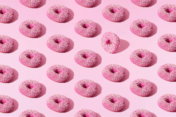 istock Arranged pink ring donuts with glaze and white crumbs on a pink pastel background. Pattern. 1379361813