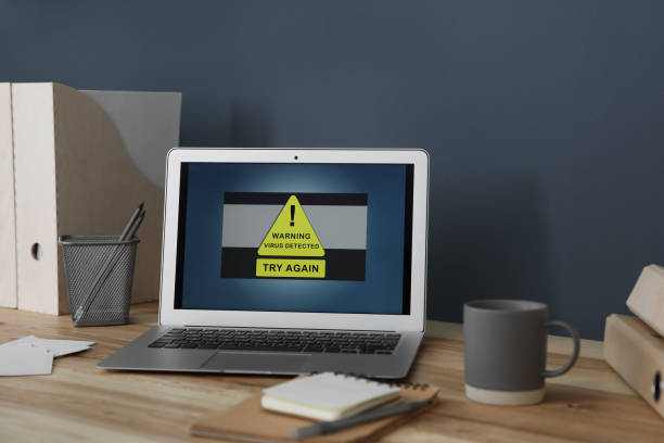 istock Laptop with warning about virus attack on wooden table in office 1379374414