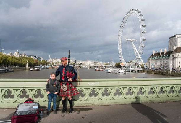 A Scottish bagpiper Posing with children for a photo, on Westminster Bridge, London, UK