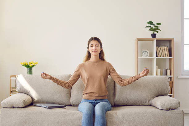ritratto di giovane donna casual calma che si rilassa e medita seduta sul divano in soggiorno. - yoga business women living room foto e immagini stock