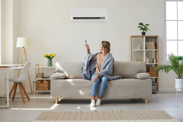Woman enjoying cool fresh air in her living room with air conditioner on the wall stock photo