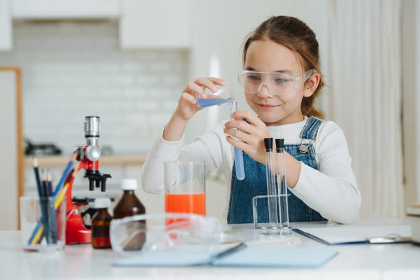 Smug little girl doing home science project, pouring blue liquid into a flask stock photo