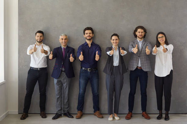 istock Business leaders showing thumbs up while standing against gray wall and looking at camera. 1379418504