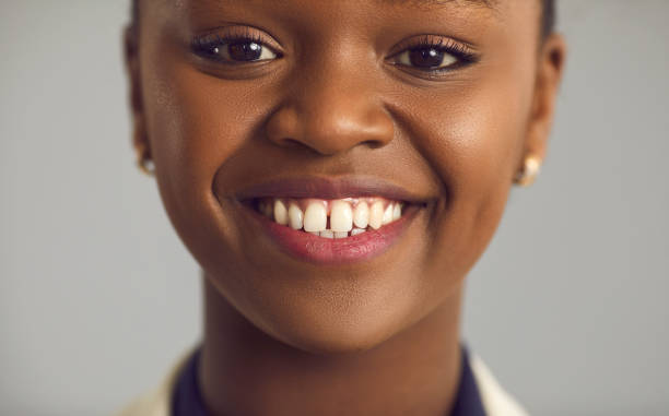 Close up portrait of a happy young black woman with a charming white toothy smile Headshot portrait of happy glad pretty young black woman with nude makeup, gap between upper front teeth and charming toothy smile. Human face, women's beauty, people's appearance, dental care concept gap toothed stock pictures, royalty-free photos & images