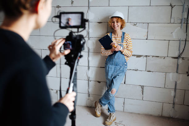 Photographer shooting a happy female construction engineer in a white helmet Photographer shooting a happy female construction engineer in a white helmet. Over a rough grey brick wall. tripod attack stock pictures, royalty-free photos & images