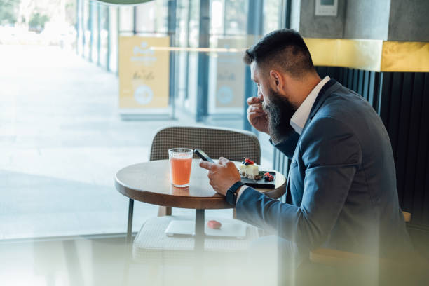 istock Handsome Business Man Using Mobile Phone While Eating Cake in the Restaurant 1379434986