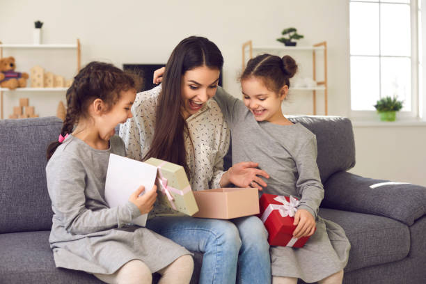 une jeune femme excitée ouvre le cadeau que ses petits enfants lui ont offert le jour de la fête des mères - fully unbuttoned photos et images de collection