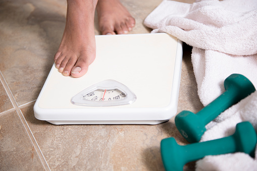 Healthy Lifestyle - African American teen steps on bathroom scale.  Her exercise weights and bath towel are on the floor next to her scale.