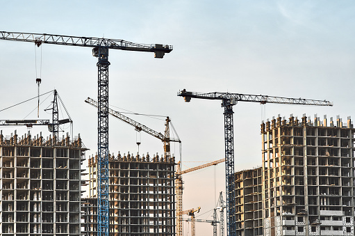 Construction site with frames of multistory buildings and cranes at clear blue sky background, evening light