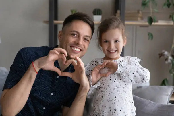 Excited dad and girl making hand hearts at camera, showing symbol of love, care, gratitude, kindness, promoting charity. Father and little daughter kid head shot portrait. Family relations concept