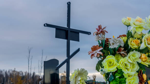 istock Metallic grave cross with artificial flowers on dramatic sky background. Orthodox traditional cemetery in snowy winter. 1379614949