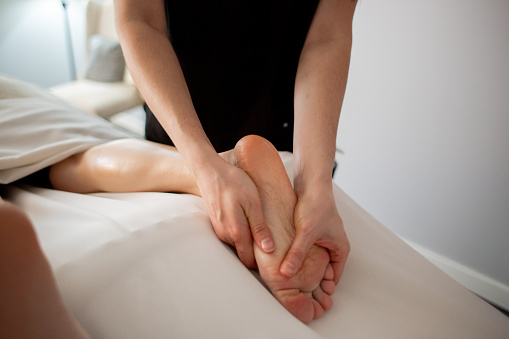 Physical therapist is using her hands to massage the feet of a female patient. Personal wellness and healthy lifestyle concepts are shown in this image.