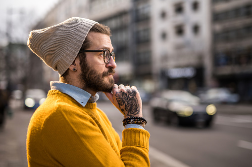 Close-up of tattooed young hipster man contemplating in the city.