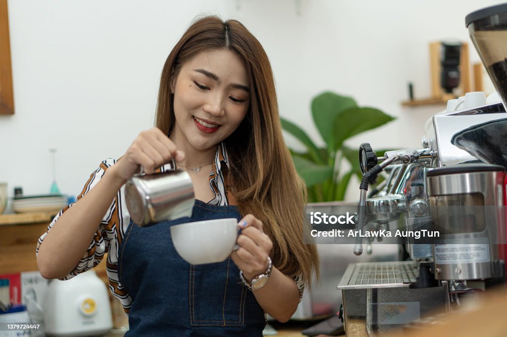 Smiling Asian female barista with coffee cup in hand Female worker pouring coffee into a cup 25-29 Years Stock Photo