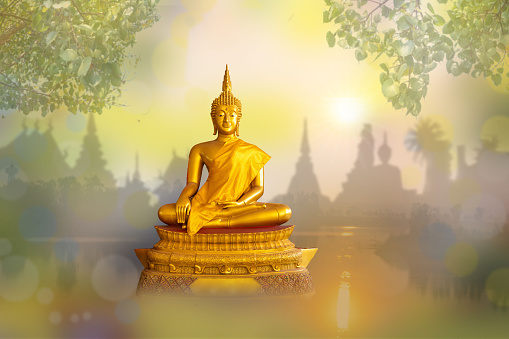 Buddha statue sitting on a river and the temple with golden sky background.