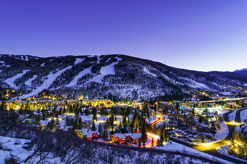 Vail Village and Lionshead Colorado Night View - Town of Vail, Colorado lit up at night in winter with ski runs on mountain above. Scenic landscape of one of Colorado's premier ski resorts.