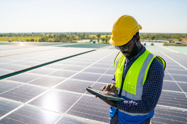 ingegnere africano che utilizza tablet digitali per la manutenzione dei pannelli solari sul tetto dell'edificio. - renewable energy power line electricity fuel and power generation foto e immagini stock