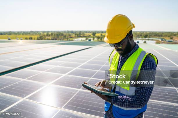 African Man Engineer Using Digital Tablet Maintaining Solar Cell Panels On Building Rooftop Stock Photo - Download Image Now