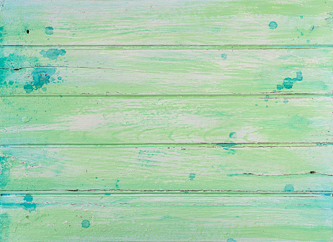 Five boards are arranged horizontally across the image. They are painted with green and turquoise paint and there are join lines between each board. All of the boards are worn and weathered and show grain, cracks, and dents in them.