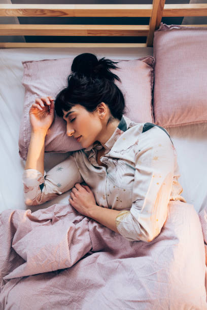 Sound Asleep: Overhead Waist Up Shot of a Pretty Woman in Pyjamas Sleeping on a Bed stock photo