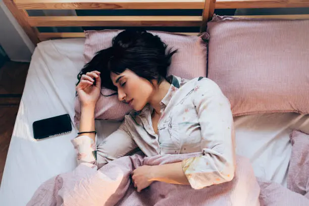 Photo of Technology-Aided Sleep: Woman in Pyjamas Listening to Relaxing Music on Her Smartphone in Bed in the Morning