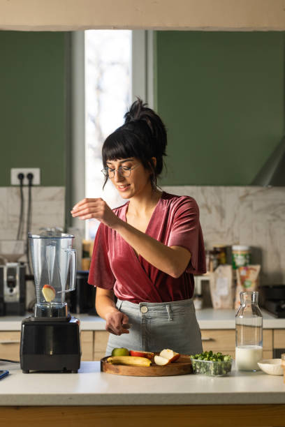 happy young woman preparing healthy breakfast at home - blender apple banana color image imagens e fotografias de stock