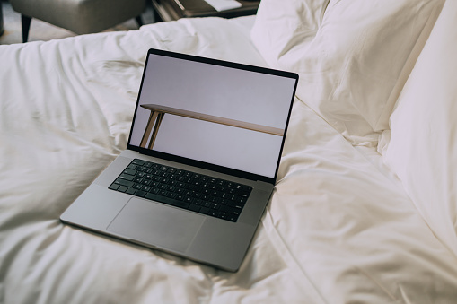 An open laptop computer on a made bed with white sheets.