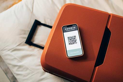 A packed suitcase and a mobile phone showing a digital covid passport QR code on a bed with white sheets.