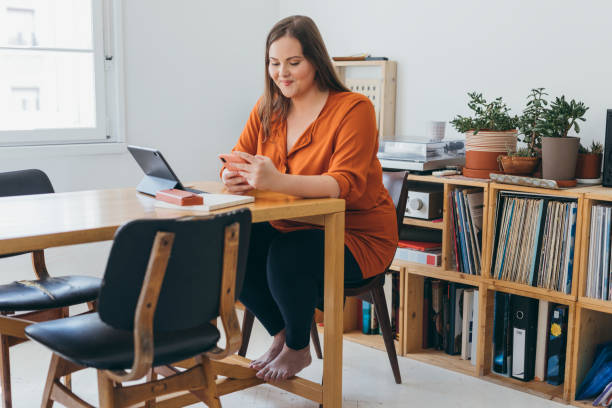 istock Smiling Plus Size Woman Using her Mobile Phone while Sitting at the Desk in her Home Office 1379816736
