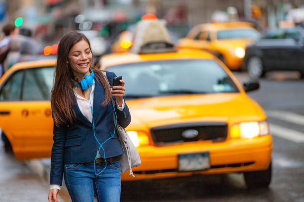 giovane donna che cammina nella città di new york usando l'app del telefono per il taxi che saluta con le cuffie che si spostano dal lavoro. ragazza asiatica felice di mandare messaggi sullo smartphone. pendolare urbano a piedi nyc - yellow taxi foto e immagini stock