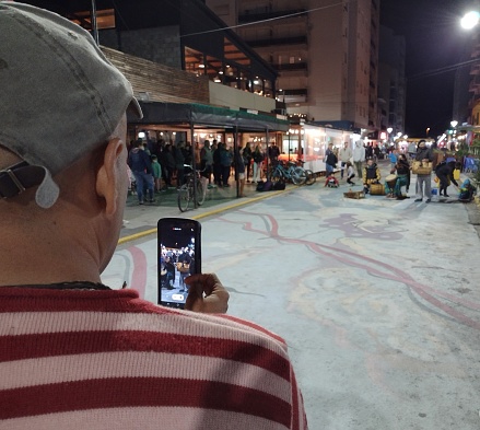 Necochea, Buenos Aires, Argentina. January 31, 2022: a man photographs streets performers with his cell phone in the night of Necochea