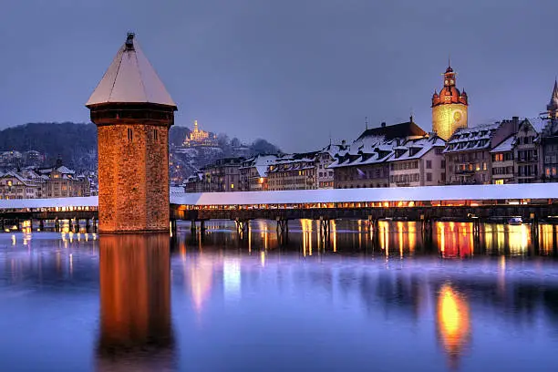 Winter-night composition of Lucerne/Luzern (Switzerland) skyline seen from Seebrucke, with the famous Chapel Bridge, the City-Hall Tower and Lucerne waterfront. On a hill in the foreground Chateau de Guetsch is visible. Winter, overcast evening recorded using HDR technique.