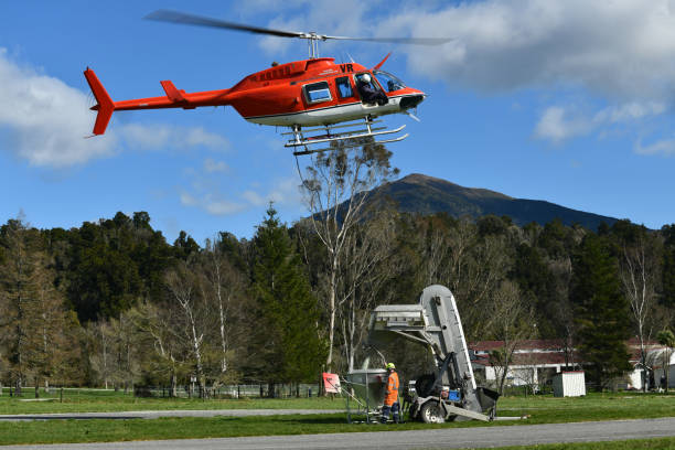 Greymouth, New Zealand,  September 2, 2021: A helicopter hovers overhead while an attendant refills a monsoon bucket with fertiliser
