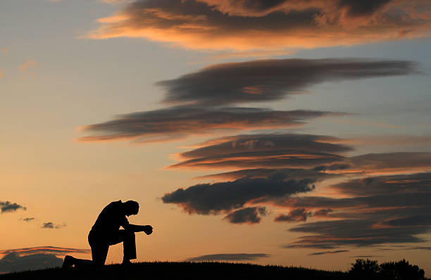 Evening Prayer Silhouette of Unrecognizable Man Kneeling stock photo