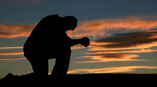 silhouette eines älteren kaukasischen männer beten - praying men god kneeling stock-fotos und bilder
