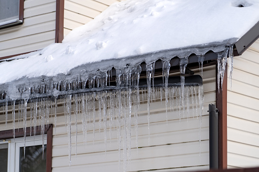 Icicles onroof of private house resulting from improper construction of roof. Metal Downpipe system, Guttering System, External downpipes and drainage pipes at winter