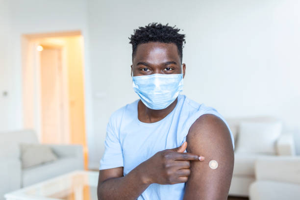 istock Vaccinated Man with protective face mask Looking At Arm With Injection Plaster, Portrait Of Vaccinated African Man Showing His Arm 1379960953