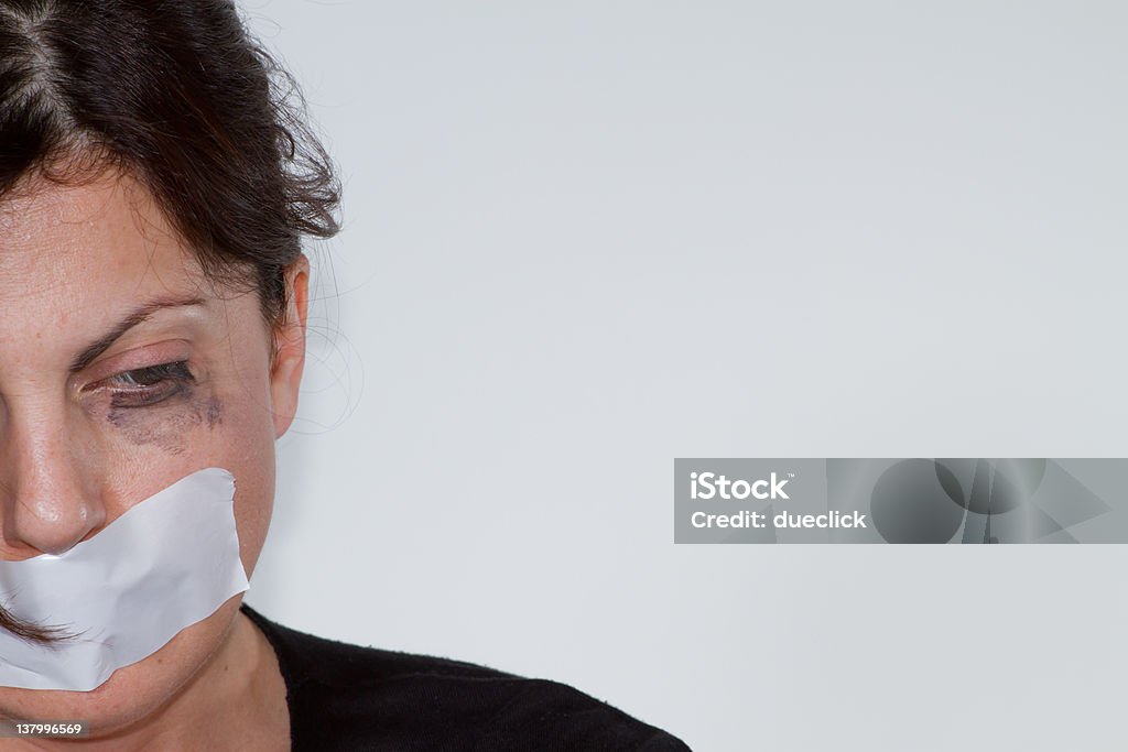 Battered woman with tape over mouth on an off-white wall Stop Violence against Women  Sexual Assault Stock Photo