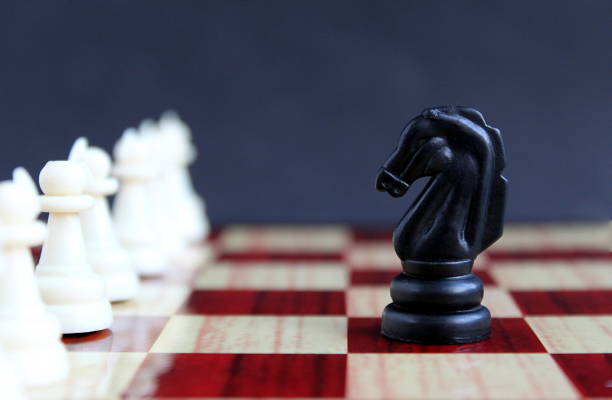 Chess piece black horse standing in front of white pawns Chess piece black horse standing in front of white pawns black knight stock pictures, royalty-free photos & images