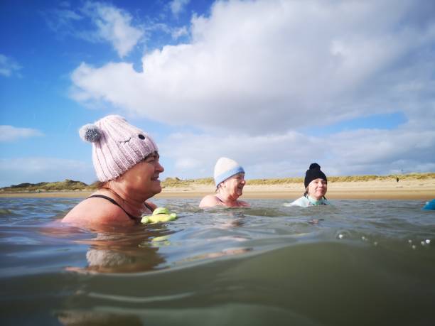 Open Water Swimmers Burry Port, Wales, UK: Febuary 25, 2022: A group of mature female friends swimming in the sea. Open or cold water swimming is a popular winter sport with many new groups across the UK. woman cold water swimming stock pictures, royalty-free photos & images