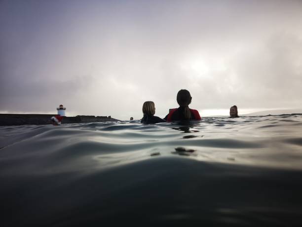 Open Water Swimming - Silhouettes Burry Port, Wales, UK: December 26, 2021: A group of mature female friends swimming in the sea. Open or cold water swimming at sunset with silhouettes at surface level. woman cold water swimming stock pictures, royalty-free photos & images