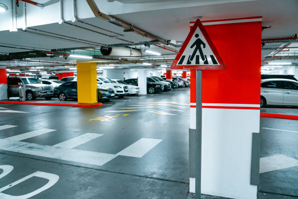 istock Parking garage underground interior, pedestrian crossing. Illuminated underground car parking interior under modern mall with lots of vehicles and arrows on floor. 1380017769