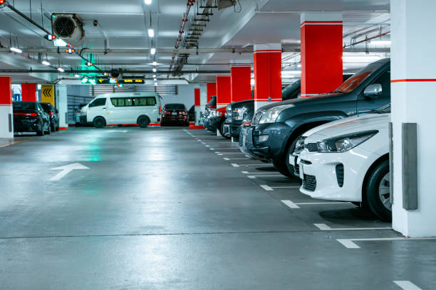 istock Parking garage underground interior, pedestrian crossing. Illuminated underground car parking interior under modern mall with lots of vehicles and arrows on floor. 1380018090