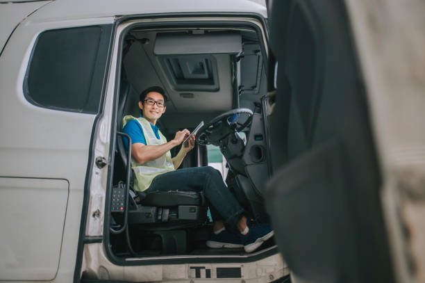 asiatischer chinesischer sattelzugfahrer, der lächelnd auf die kamera schaut, indem er ein digitales tablet verwendet, das die lieferplanliste aktualisiert - computer manual worker truck driver truck stock-fotos und bilder