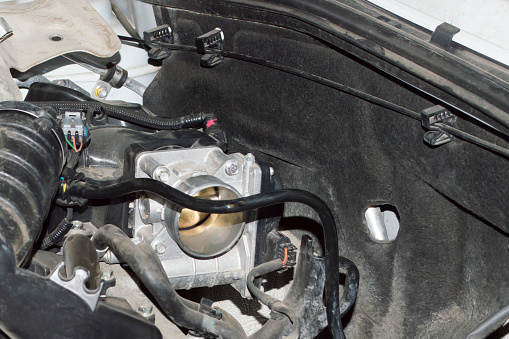 View of the throttle valve installed under the hood of a white car