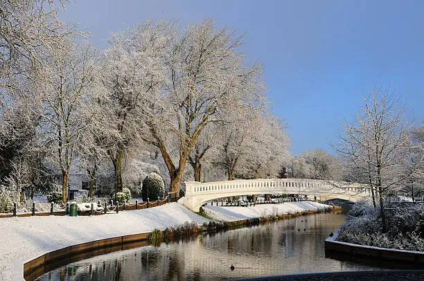 A view of a river running through a park in winter covered in snow. XL image size.