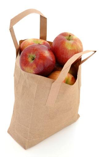 Apple fruit in a brown paper recycled carrier bag  over white background, red dessert variety.