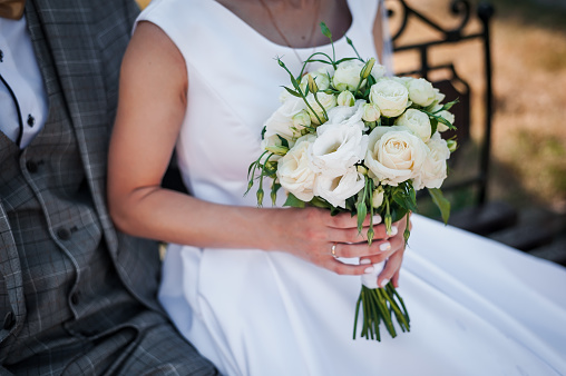 wedding bouquet of white and pink roses and peonies in the hands of the bride on the background of a white dress
